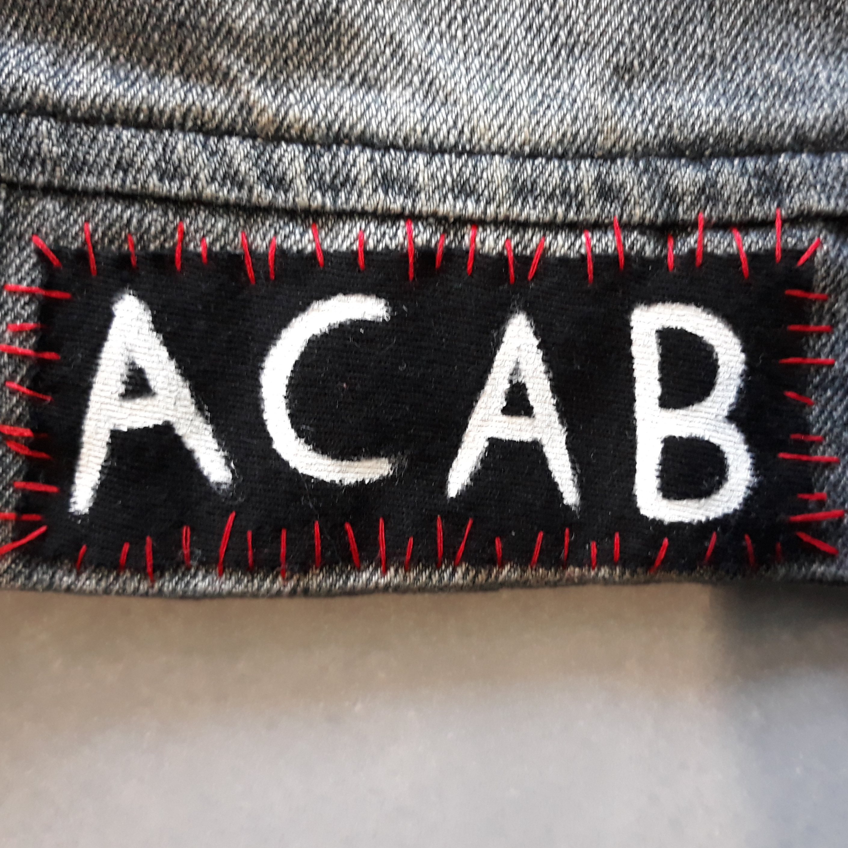 A patch with 'ACAB’ written in white. It is sewn on with red thread.